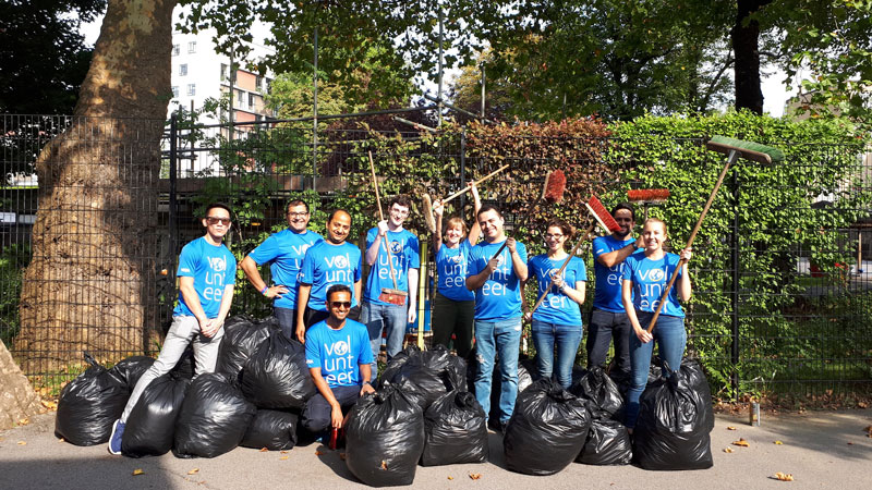 A group of Visa volunteers, holding brooms, pose in front of full garbage bags.