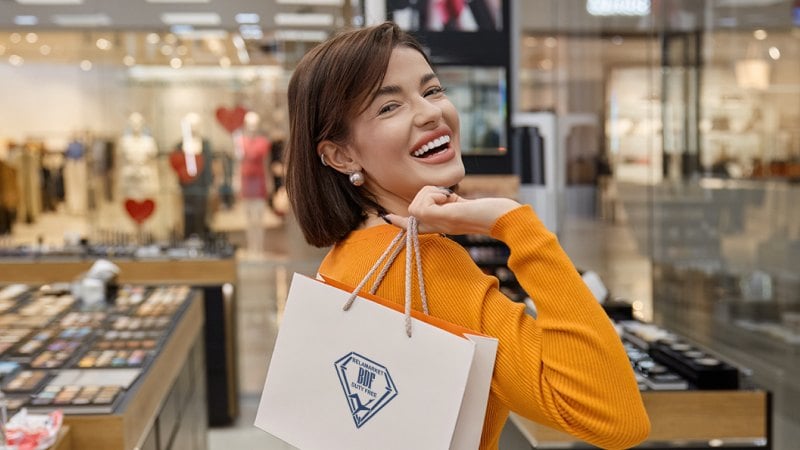Улыбающаяся женщина в оранжевом свитере стоит с сумкой для покупок в торговом центре