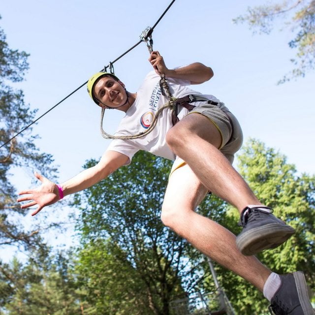 Человек в шлеме и страховочном ремне с удовольствием катается на тролле на тросе через лес