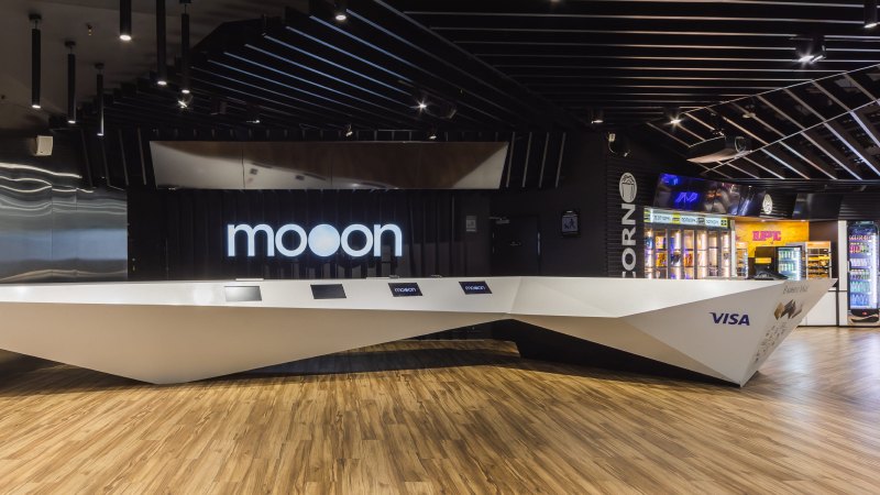 Просторная современная зона приема с элегантным белым столом с четкими углами на темном фоне. На стене светится надпись «Moon».