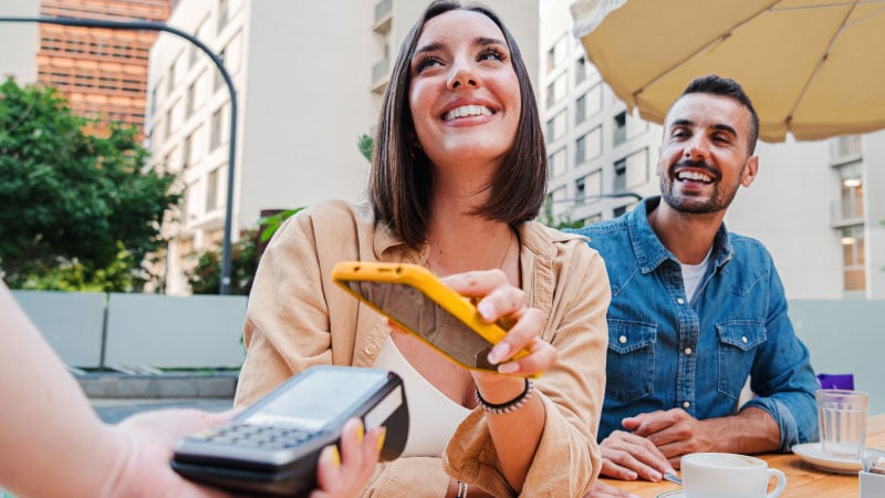 A woman is going to pay by phone, a person is sitting next to her.
