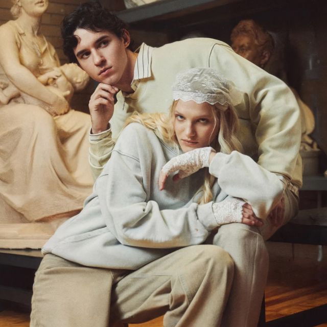 Женщина и мужчина в светлой одежде сидят рядом в художественной студии, окруженные скульптурами