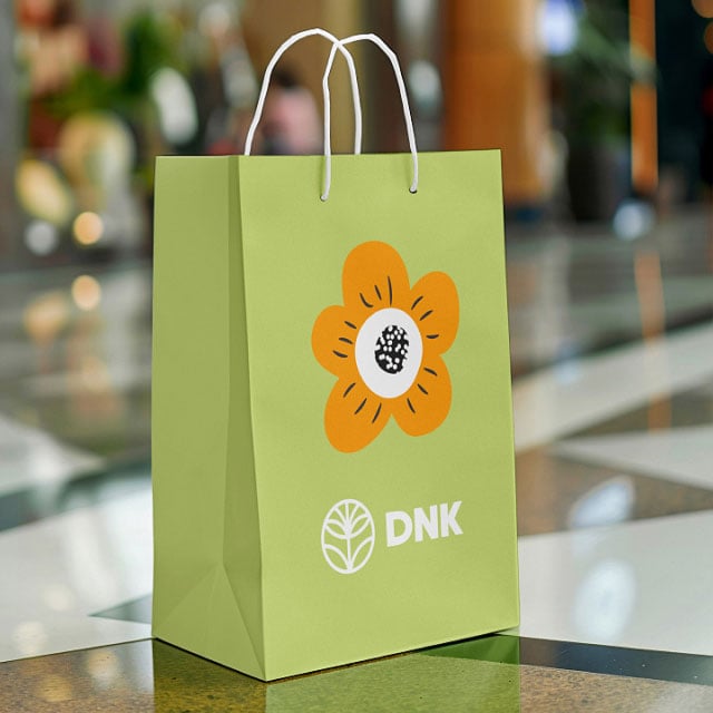 Светло-зеленый пакет для покупок с белой ручкой украшен оранжевым цветочным узором и логотипом «DNK».